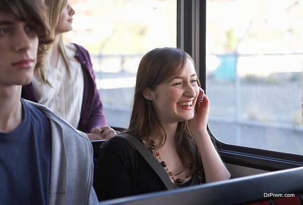 Young woman using mobile phone on bus, smiling