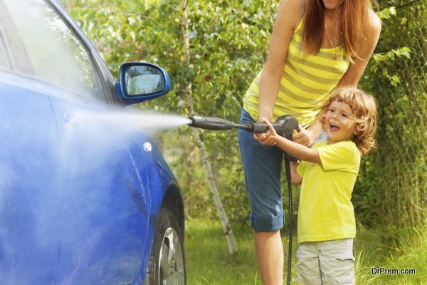 Mother and three years old son washing car with high pressure washer with boy pointing water nozzle  standing in outside in the yeard parking