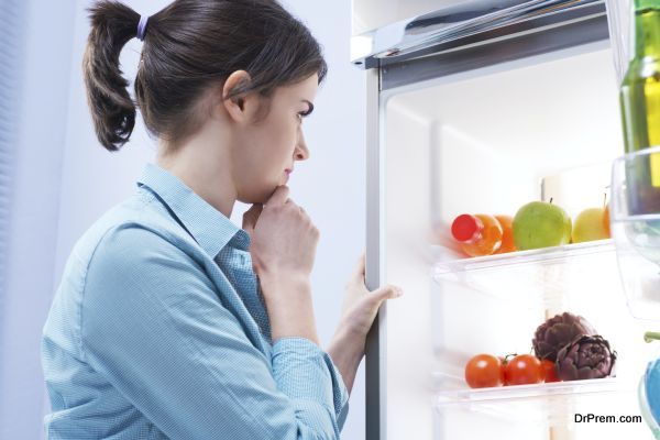 Young pensive woman looking in the refrigerator with hand on chin.