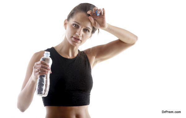Sporty yoga girl on white background holding a bottle of water, wiping sweat from forehead after practice