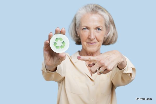 Portrait of senior woman holding badge with recycling symbol against blue background