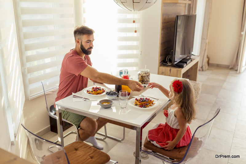 Young father and beautiful little daughter sitting at dinning room table, having breakfast