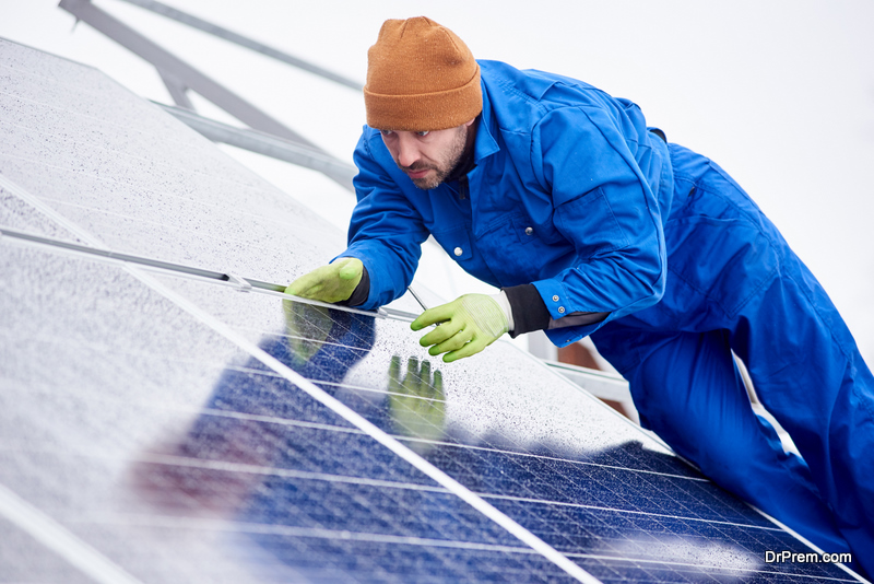 Man installs solar batteries using tools on the roof in winter. He dressing uniforms and gloves. Close-up