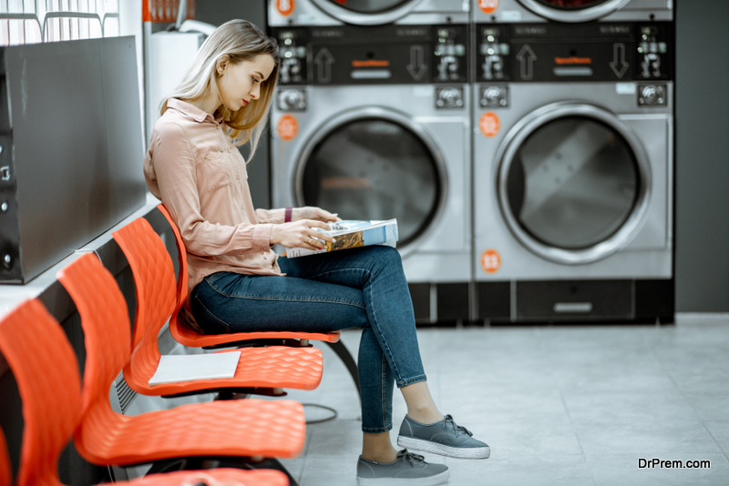 Young woman waiting for the clothes to be washed sitting on the chair at the self-service laundry